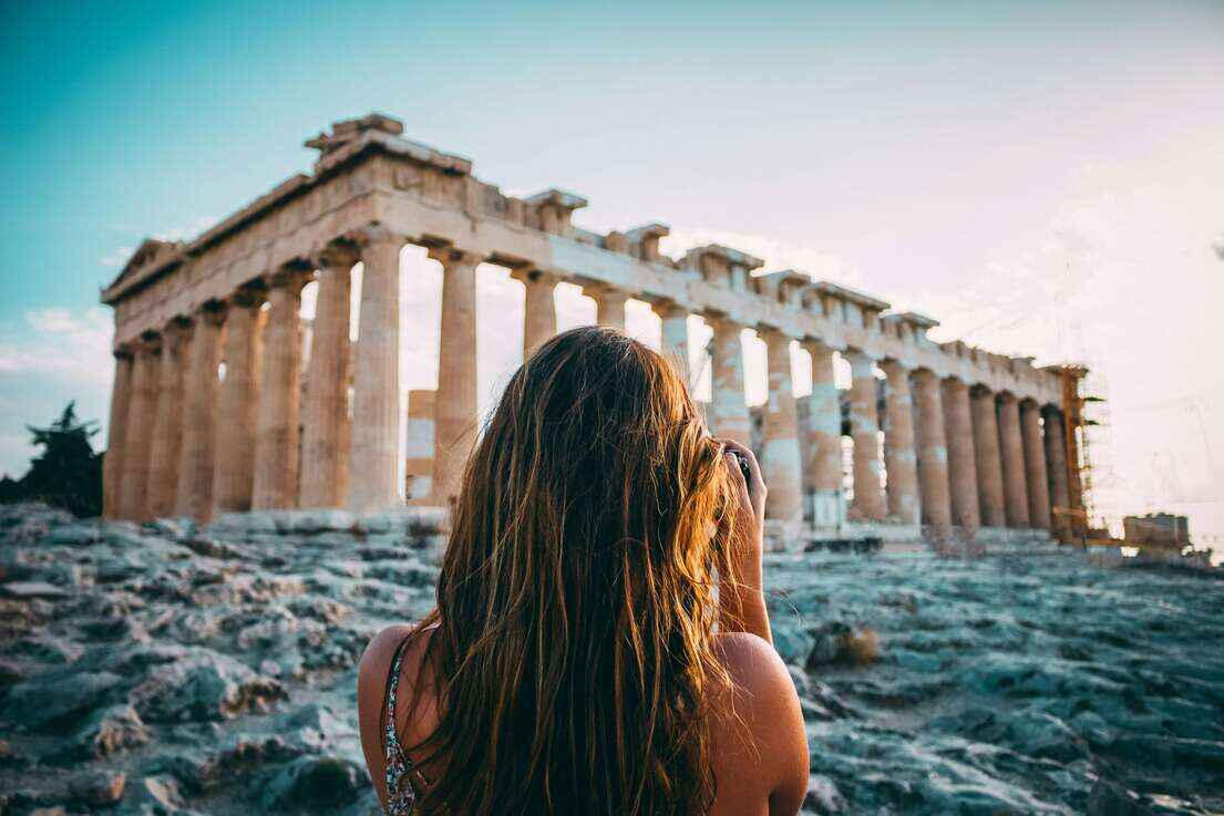 Woman taking a photo of the Parthenon on the Acropolis in Athens, Greece at sunset