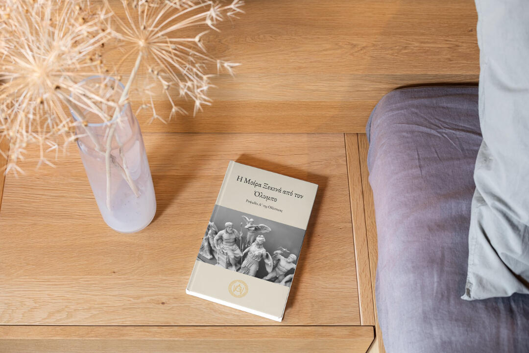 Modern Greek learning paperback book placed on a wooden table near a bed — officially printed edition available on Amazon
